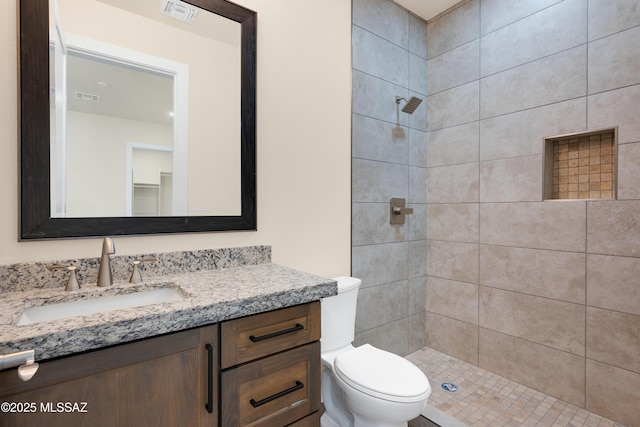 bathroom with toilet, vanity, visible vents, and a tile shower