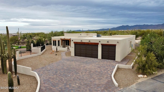 pueblo revival-style home featuring an attached garage, fence, decorative driveway, a mountain view, and stucco siding