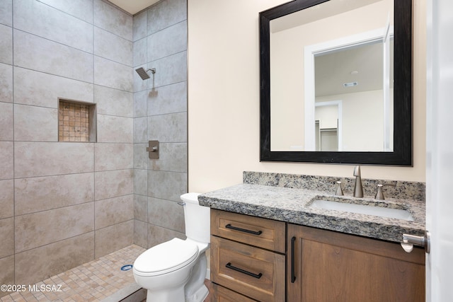 full bath with toilet, tiled shower, visible vents, and vanity