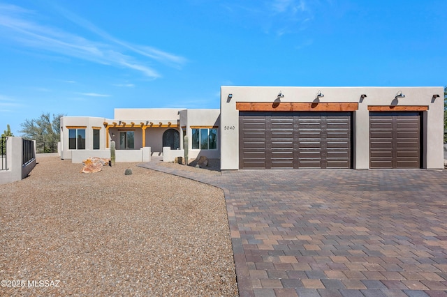 adobe home featuring a garage, fence, decorative driveway, and stucco siding