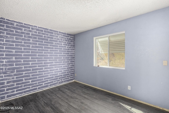 empty room featuring baseboards, a textured ceiling, wood finished floors, and brick wall