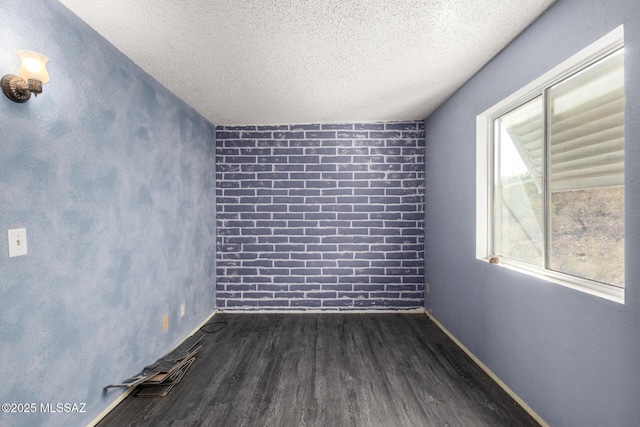 unfurnished room featuring dark wood-type flooring, baseboards, brick wall, and a textured ceiling