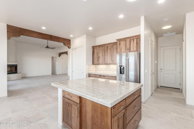 kitchen with a large fireplace, a kitchen island, high end fridge, backsplash, and brown cabinetry