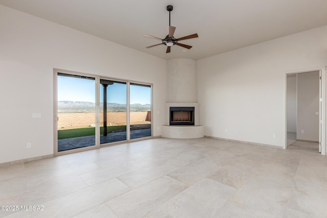 unfurnished living room featuring a ceiling fan, a fireplace, a towering ceiling, and baseboards