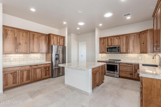 kitchen featuring brown cabinetry, a kitchen island, backsplash, stainless steel appliances, and a sink