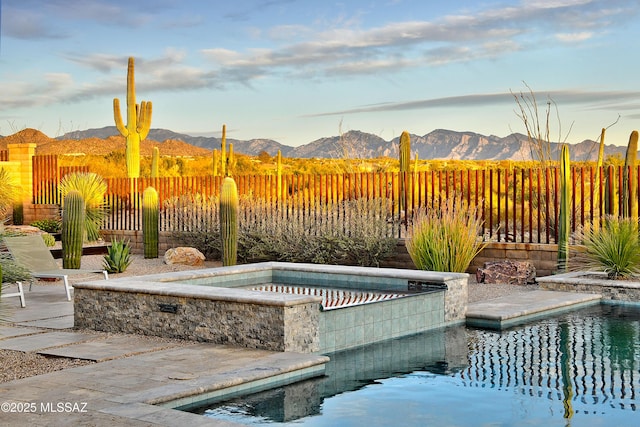 outdoor pool with an in ground hot tub, a fenced backyard, and a mountain view