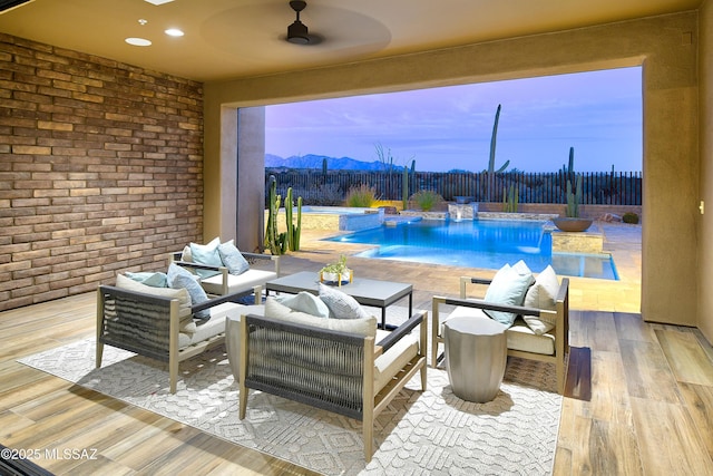 view of pool featuring a mountain view, outdoor lounge area, a fenced backyard, and a ceiling fan