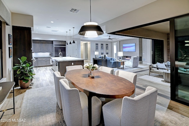 dining room featuring light wood-style floors, a lit fireplace, visible vents, and recessed lighting