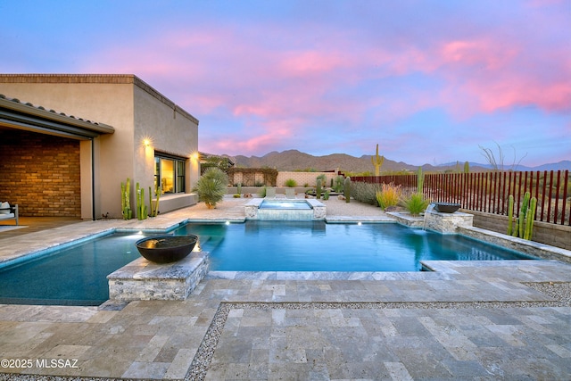 pool at dusk with a patio, a pool with connected hot tub, a fenced backyard, and a mountain view