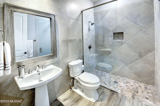 full bathroom featuring a tile shower, tile walls, toilet, and wood finished floors