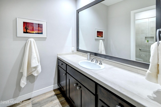 bathroom with a shower, wood finished floors, vanity, and baseboards