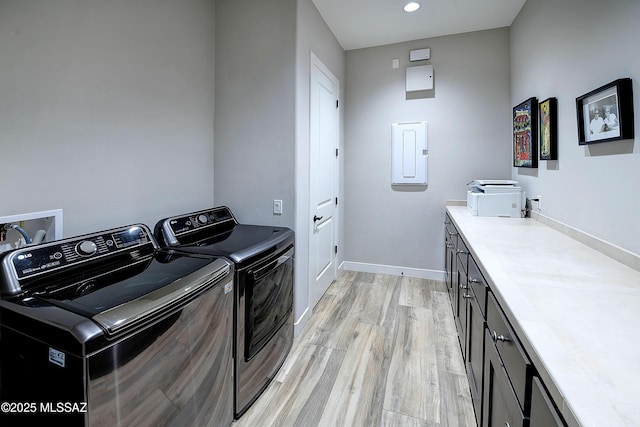 clothes washing area with light wood-style flooring, baseboards, electric panel, cabinet space, and washer and clothes dryer