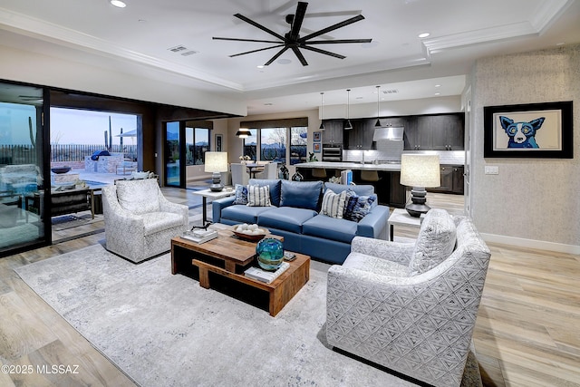 living area featuring light wood finished floors, a raised ceiling, and crown molding