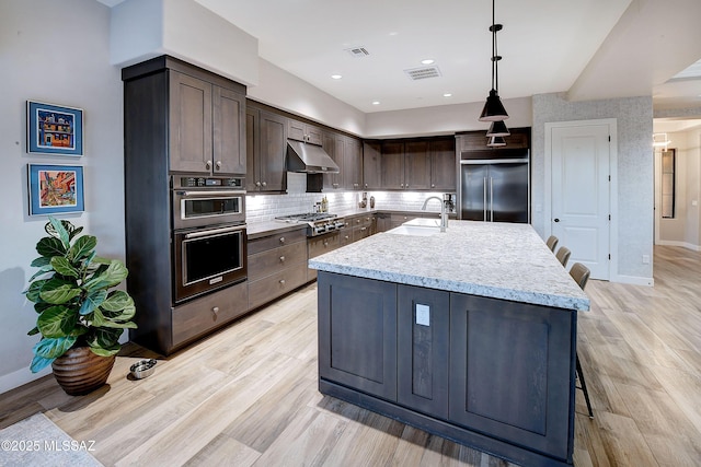 kitchen with decorative light fixtures, visible vents, multiple ovens, under cabinet range hood, and built in refrigerator