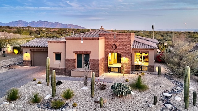 view of front facade featuring decorative driveway, a tile roof, stucco siding, an attached garage, and a mountain view