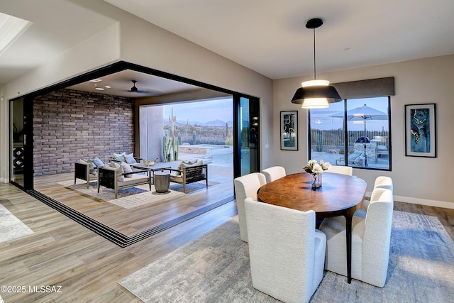 dining room with a ceiling fan, brick wall, baseboards, and wood finished floors