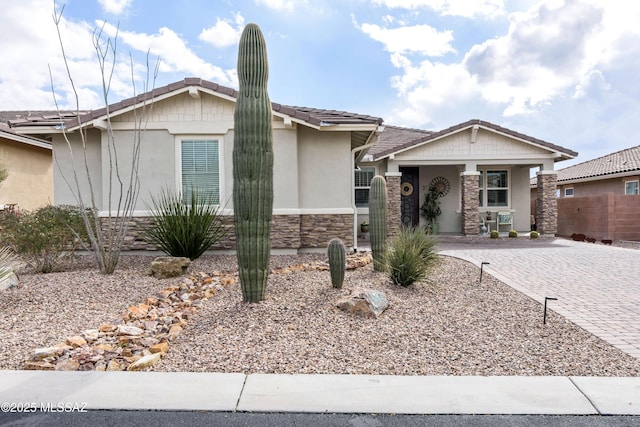 view of front of house with stone siding, a tile roof, fence, decorative driveway, and stucco siding