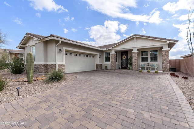 view of front of house featuring a garage, fence, stone siding, decorative driveway, and stucco siding