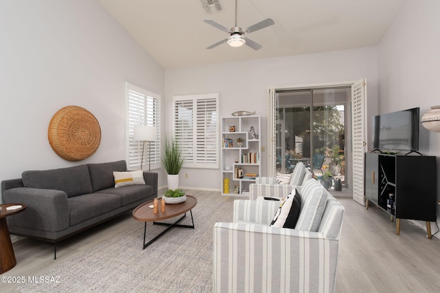 living area featuring ceiling fan, light wood-style flooring, visible vents, baseboards, and vaulted ceiling