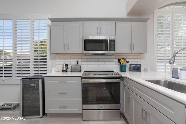 kitchen featuring appliances with stainless steel finishes, beverage cooler, light countertops, and gray cabinetry