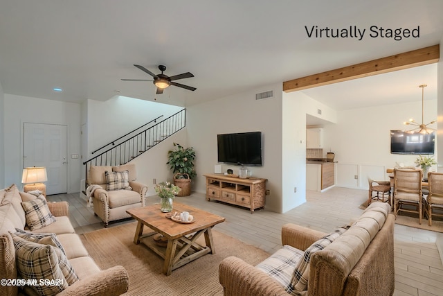 living room featuring visible vents, beamed ceiling, stairs, light wood-type flooring, and ceiling fan with notable chandelier