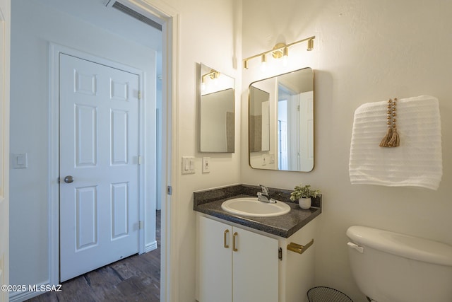 half bathroom with toilet, visible vents, wood finished floors, and vanity