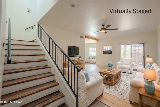 living area with visible vents, stairs, a ceiling fan, and wood finished floors