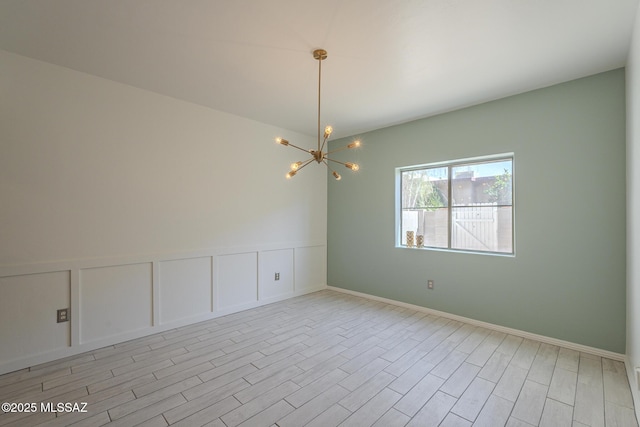 spare room featuring light wood-type flooring, a decorative wall, and an inviting chandelier