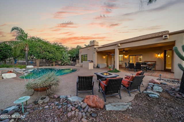 pool at dusk featuring a fire pit, ceiling fan, and a patio area