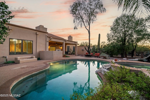 pool at dusk featuring an in ground hot tub and a patio area