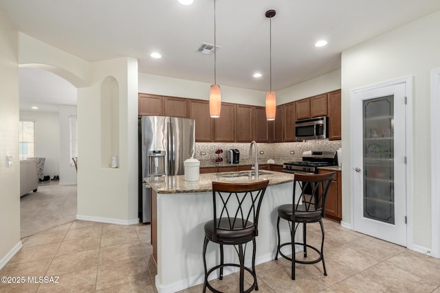 kitchen featuring a center island with sink, stainless steel appliances, pendant lighting, sink, and a kitchen bar