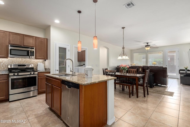kitchen featuring appliances with stainless steel finishes, sink, light stone counters, hanging light fixtures, and a kitchen island with sink