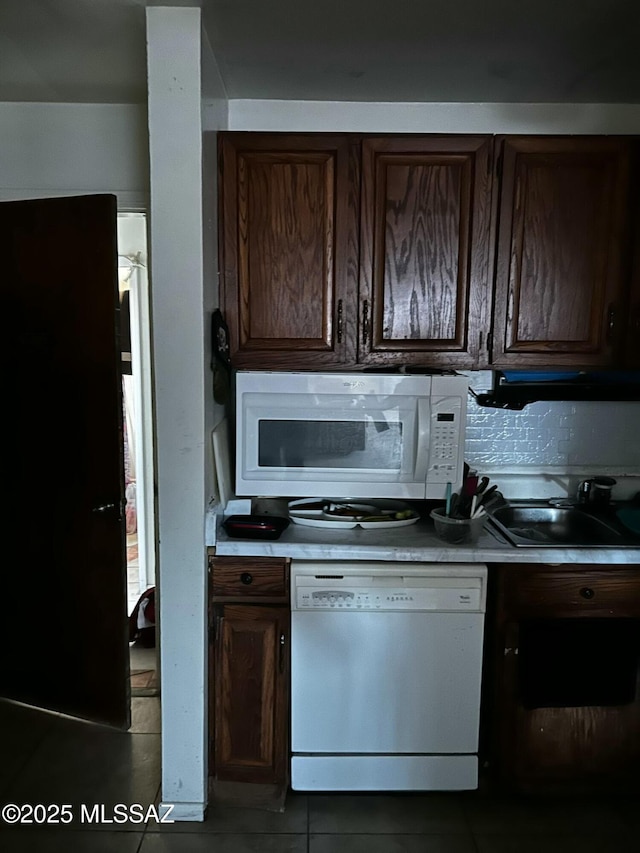 kitchen featuring white appliances, light countertops, a sink, and dark brown cabinets