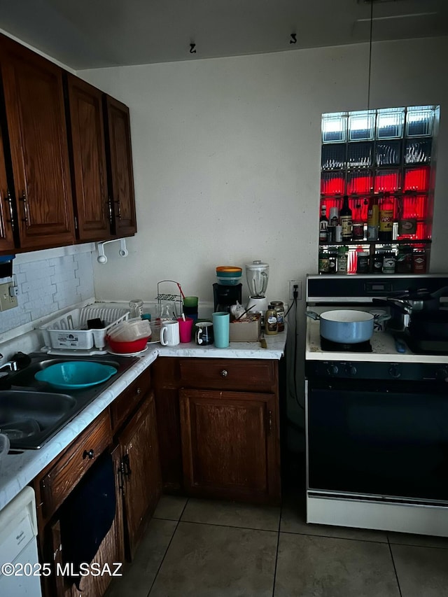 kitchen featuring light tile patterned floors, a sink, black stove, light countertops, and decorative backsplash