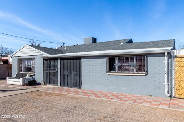 exterior space with brick siding, fence, and roof with shingles