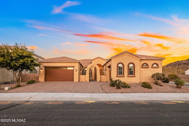 mediterranean / spanish house featuring fence, stucco siding, a garage, a tile roof, and decorative driveway