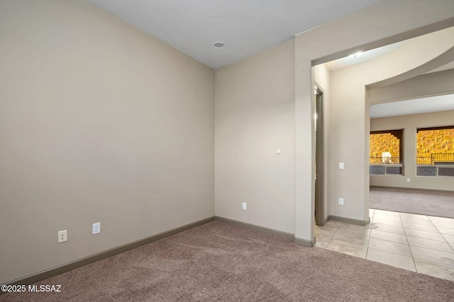 empty room with light tile patterned floors, light colored carpet, and baseboards