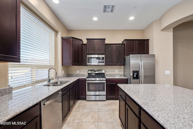 kitchen with visible vents, a sink, light stone counters, stainless steel appliances, and dark brown cabinets