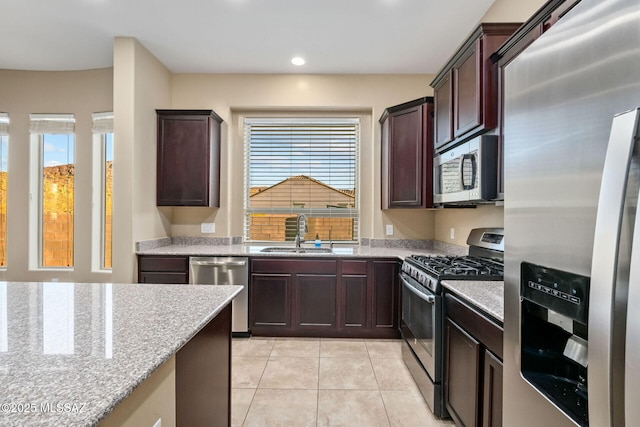 kitchen featuring light stone countertops, dark brown cabinetry, light tile patterned floors, appliances with stainless steel finishes, and a sink