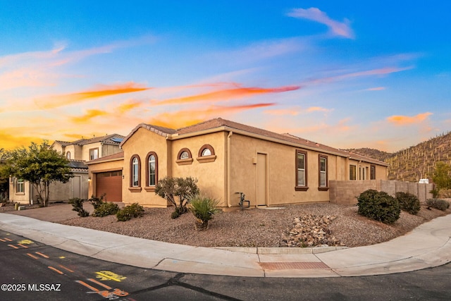 view of front of property featuring fence, a tile roof, stucco siding, driveway, and an attached garage