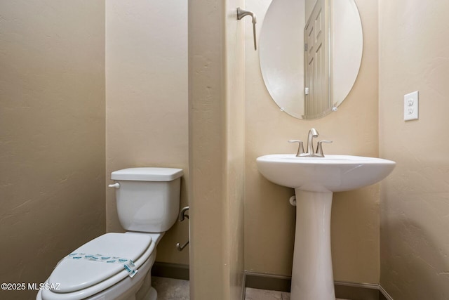 half bathroom featuring a sink, toilet, and a textured wall