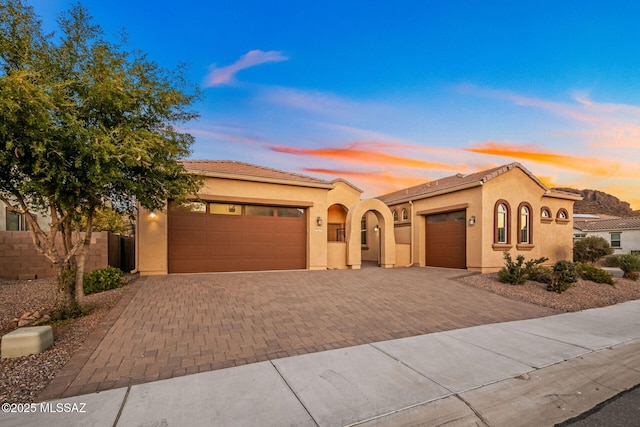 mediterranean / spanish house featuring decorative driveway, an attached garage, and stucco siding