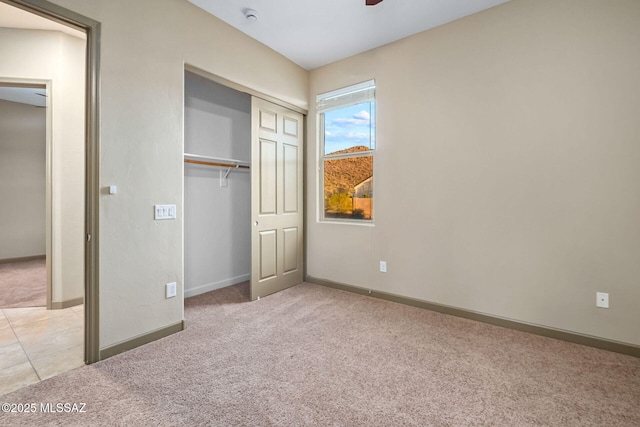 unfurnished bedroom featuring baseboards, ceiling fan, light colored carpet, light tile patterned flooring, and a closet