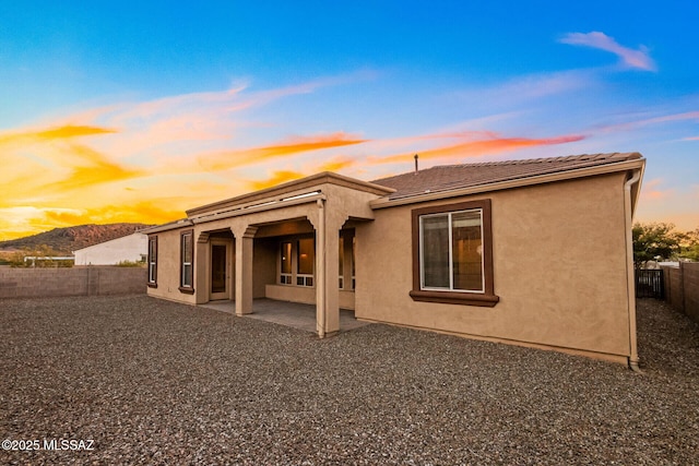 back of property at dusk featuring a fenced backyard, stucco siding, a tile roof, a patio area, and a mountain view