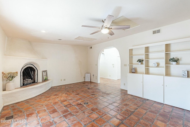 unfurnished living room with a fireplace, arched walkways, visible vents, and ceiling fan