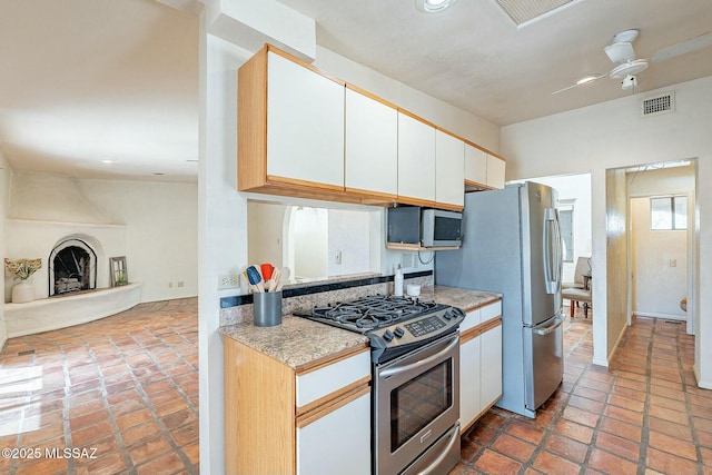 kitchen featuring visible vents, a large fireplace, ceiling fan, light countertops, and appliances with stainless steel finishes