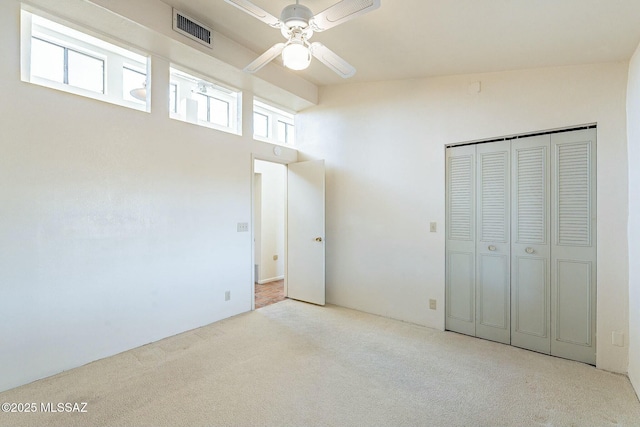 unfurnished bedroom featuring a ceiling fan, visible vents, a closet, a towering ceiling, and carpet flooring