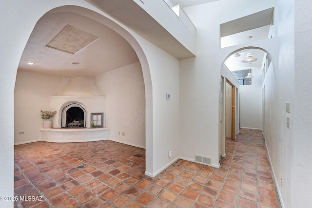 hallway featuring arched walkways, visible vents, tile patterned flooring, and baseboards