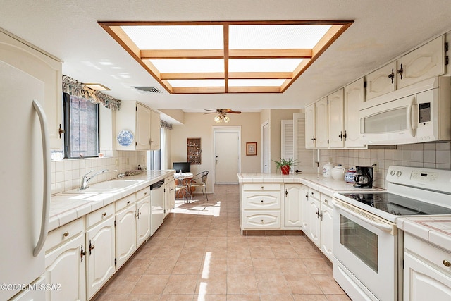 kitchen featuring tile countertops, a peninsula, white appliances, a sink, and visible vents