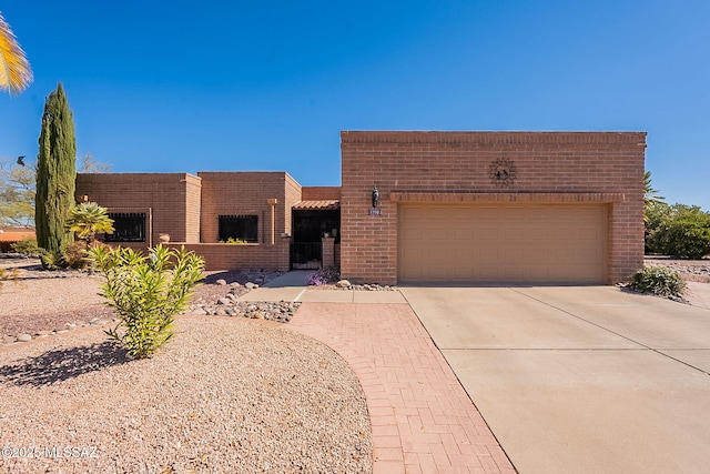 pueblo-style house featuring a garage, concrete driveway, and brick siding